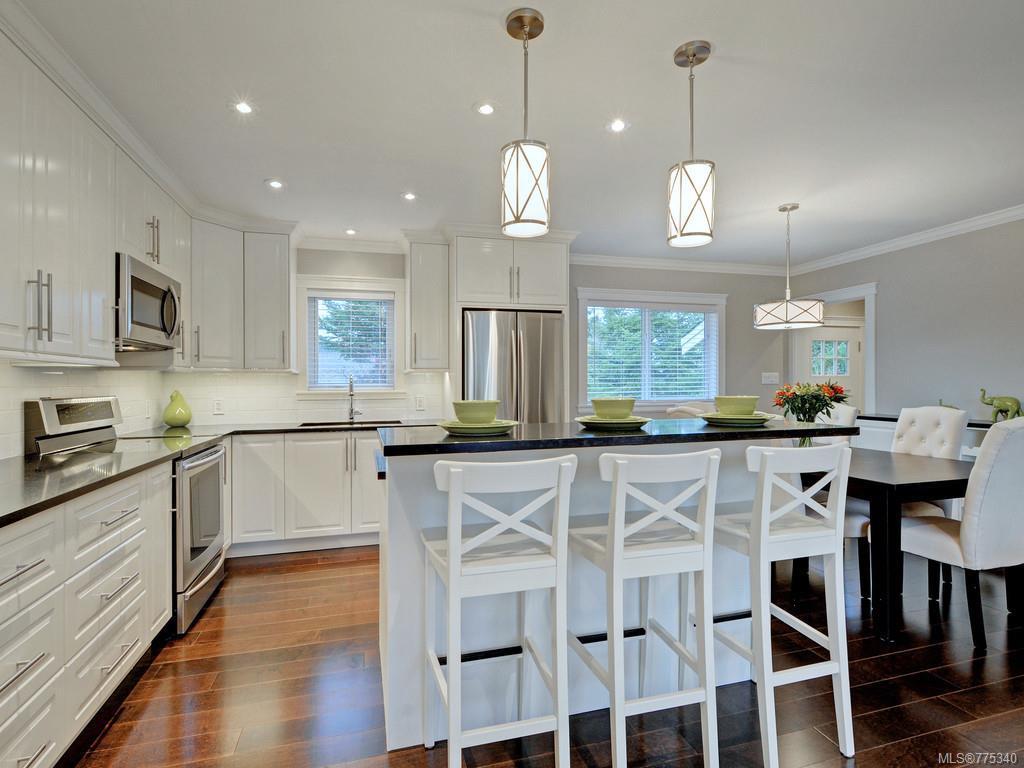 A modern and clean kitchen with white cabinets, dark countertops, stainless steel appliances, and an island with white stools.